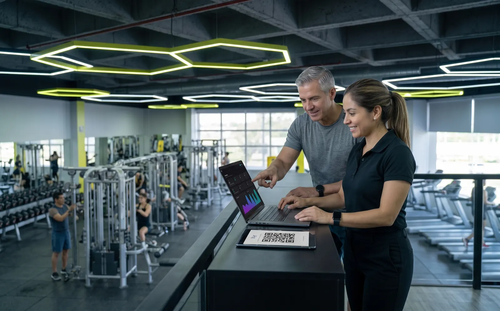 Dueña de gimnasio y gerente revisando el panel de administración en una laptop sobre el piso de entrenamiento